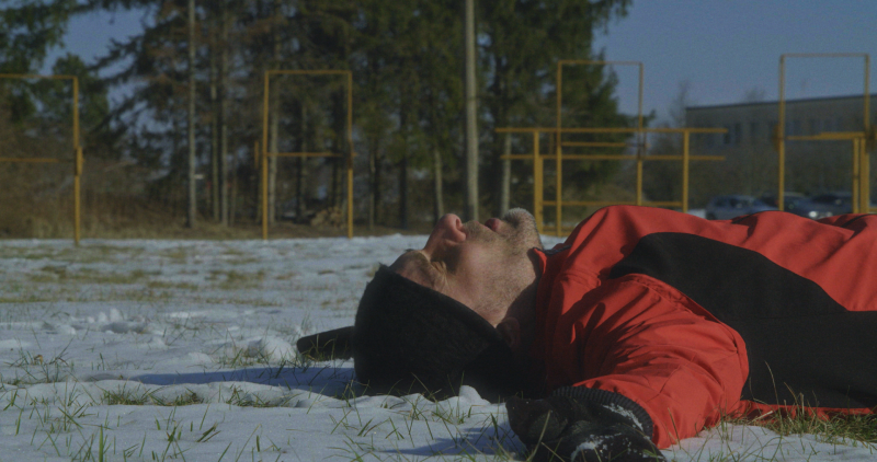 Vīrietis aizvērtām acīm guļ uz muguras sniegotā laukā.