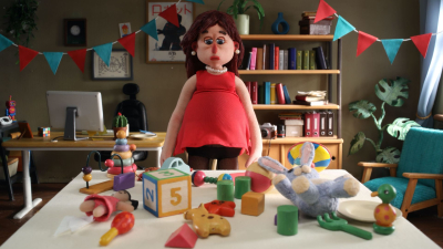 Puppet animation scene of a pregnant woman standing behind a table covered with children’s toys.