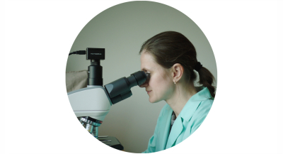 Sieviete profilā skatās mikroskopā.