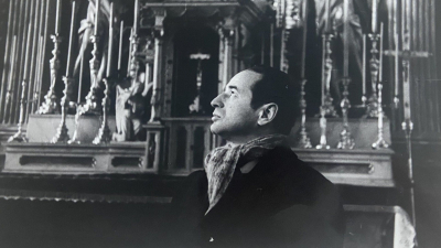 Black-and-white portrait of Herz Frank inside a church, looking upward toward an altar.
